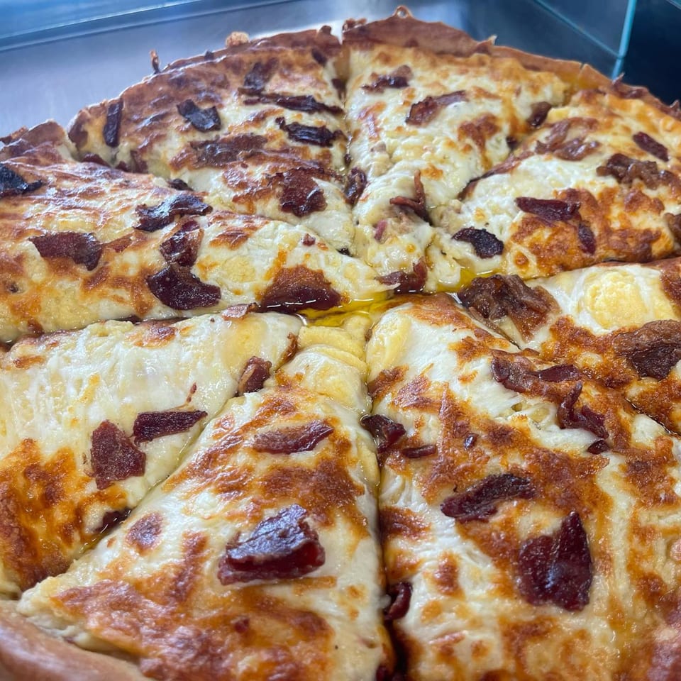 Close-up of a savory donut pizza, topped with melted cheese and crispy bacon bits.