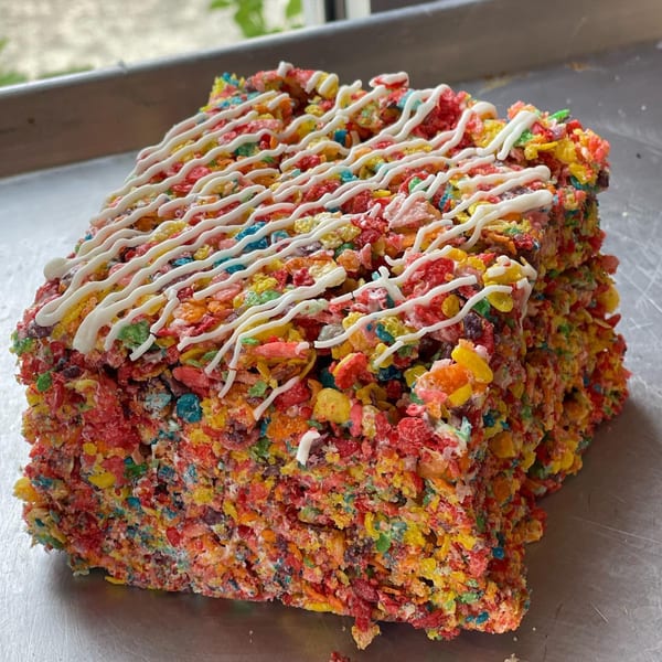 A colorful Fruity Pebbles treat with white icing drizzle sits on a metal tray.
