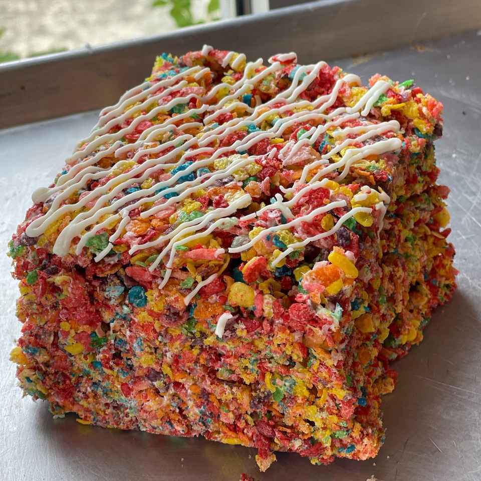 A colorful Fruity Pebbles treat with white icing drizzle sits on a metal tray.