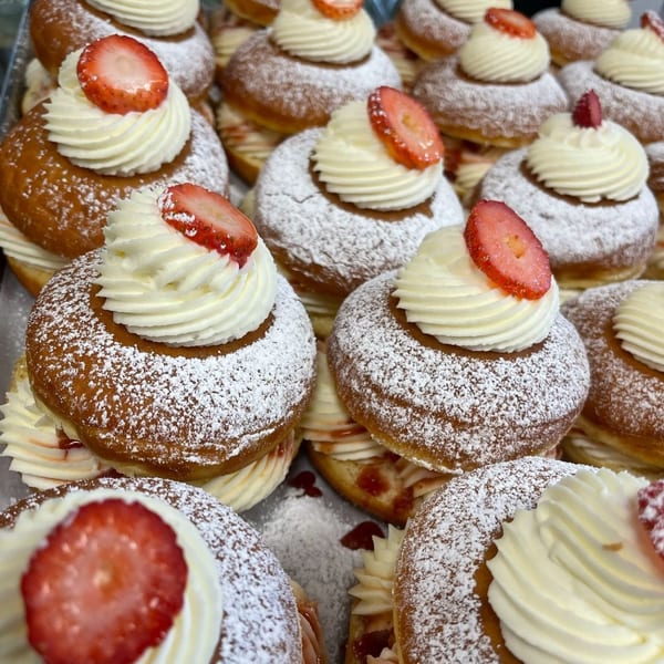Close-up of numerous strawberry cream donuts from The Donut Factory, dusted with powdered sugar.