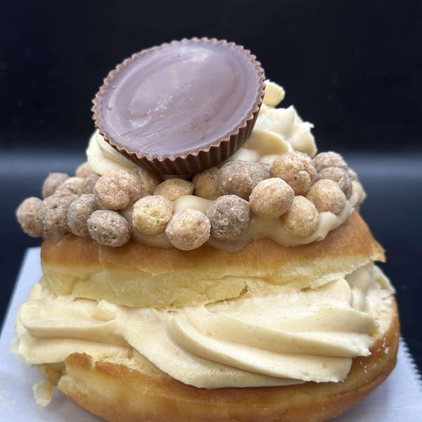A Donut Factory donut with peanut butter frosting, cereal, and a peanut butter cup on top.