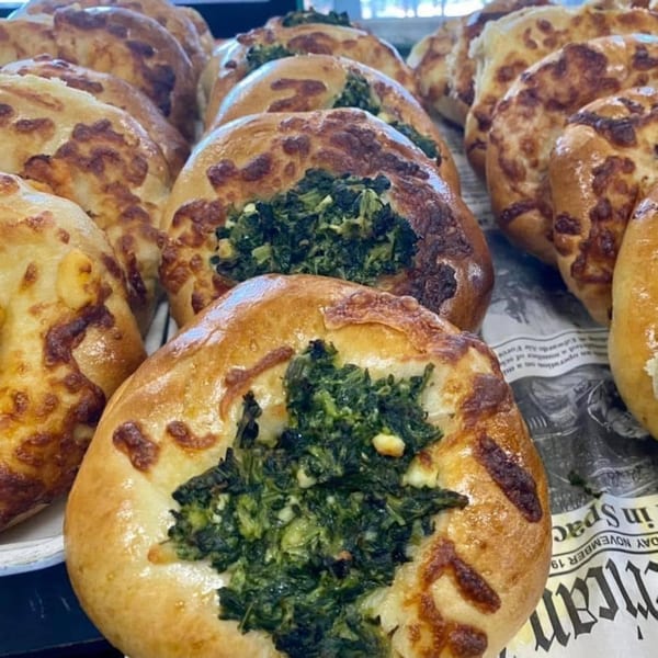 Close-up of savory pastries with golden-brown crusts and green spinach filling, some with cheese.
