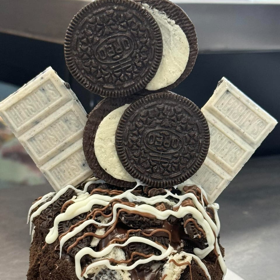 A Donut Factory donut topped with Oreo cookies, Hershey's white chocolate, and chocolate drizzle.