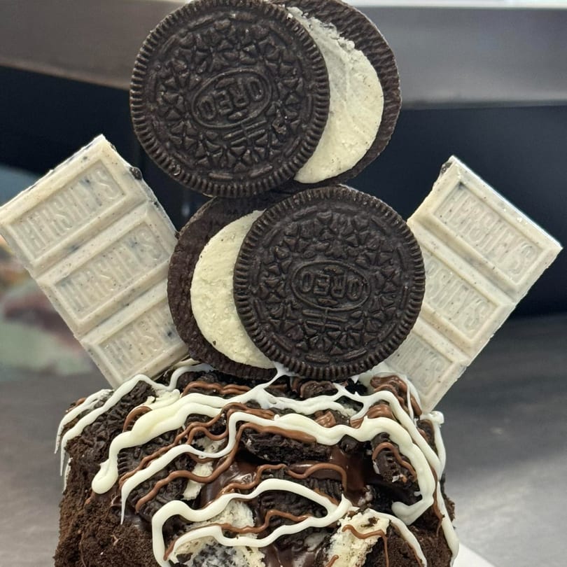 A Donut Factory donut topped with Oreo cookies, Hershey's white chocolate, and chocolate drizzle.