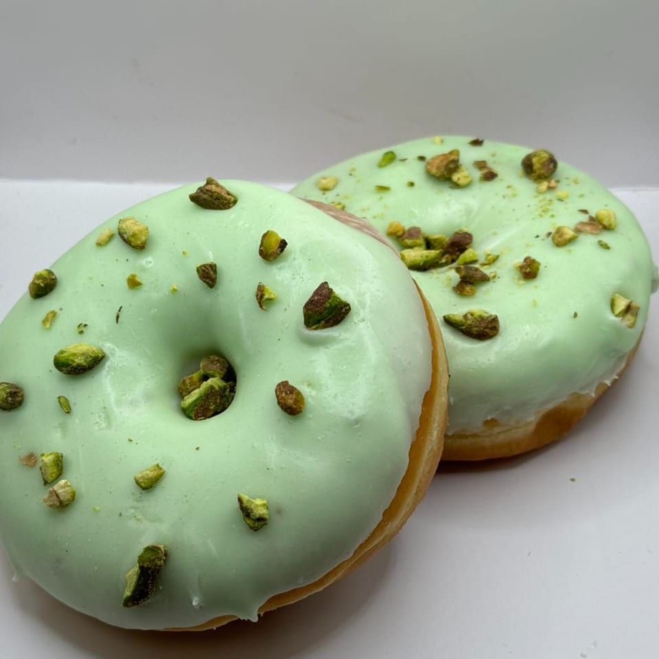 Two pistachio donuts from The Donut Factory, topped with light green icing and chopped pistachios.