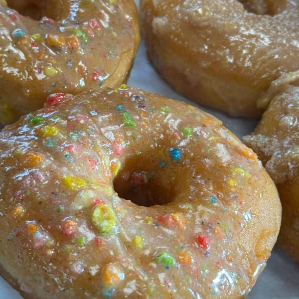 Close-up of several glazed donuts from The Donut Factory, topped with colorful cereal pieces.