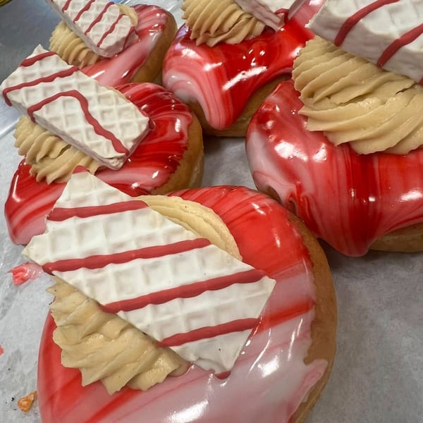 Close-up of Donut Factory donuts with red and white marbled icing, topped with cream and striped wafers.