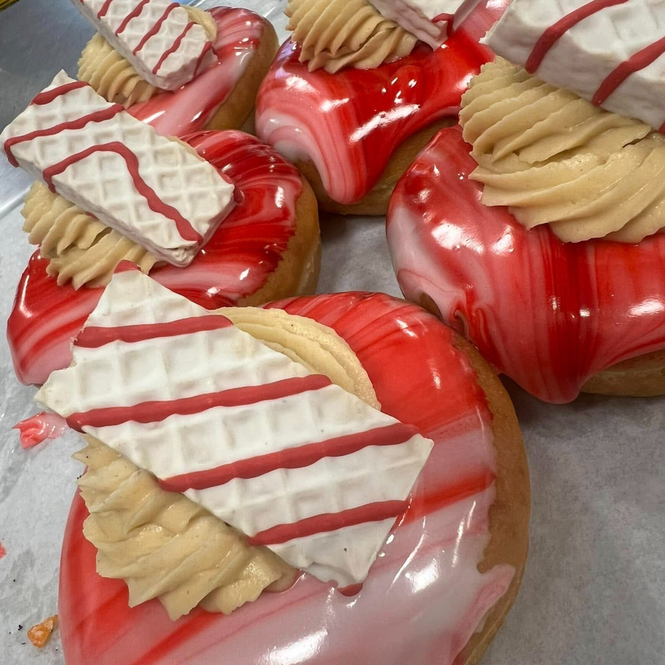 Close-up of Donut Factory donuts with red and white marbled icing, topped with cream and striped wafers.